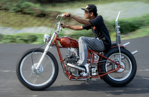AA-41 Man in a cap riding a red custom chopper motorcycle on a paved road with blurred background.