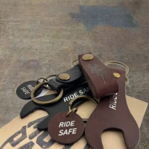 Brown leather keychain pieces and round tags reading 'Ride Safe' on a stack of keys and a tan surface.