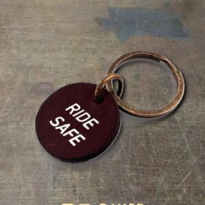 Brown circular key tag with white text 'RIDE SAFE' attached to a metal keyring on a grey surface.